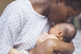 A mother in a hospital gown kisses her baby's head.
