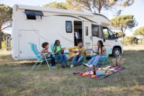 People sit outside of an RV for a picnic.
