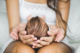 A woman holds a baby in her lap with the top of its head facing the camera.