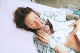 Smiling mother in a hospital bed holds a baby.