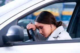 A tired driver rests their head on the steering wheel of their car.