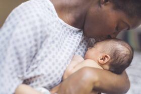 Mother in a hospital gown kisses her baby's head.