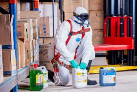 Person wearing protective gear handles bottles of chemicals in a warehouse.